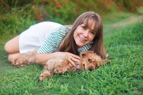 Woman joyfully posing in the grass with her dog, exuding friendliness and joy
