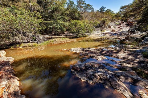 A shallow watercourse snakes through rocks and green vegetation under a blue sky, a small river