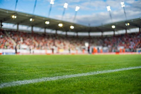 Professional soccer field with green grass and blurred stadium crowd under bright floodlights,