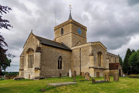 Full view of the medieval St James the Great parish church and its churchyard gravestones under a