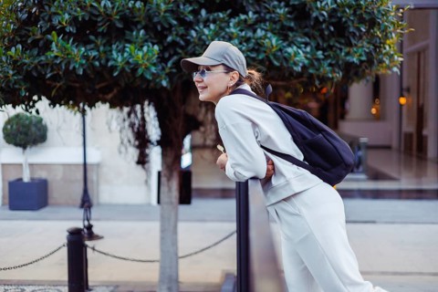 Middle-aged woman, dressed casually in light clothing, leans against a railing in an urban area.
