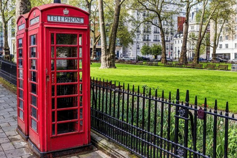 Red telephone boxes stand beside the railings of Berkeley Square Gardens amid historic London Plane