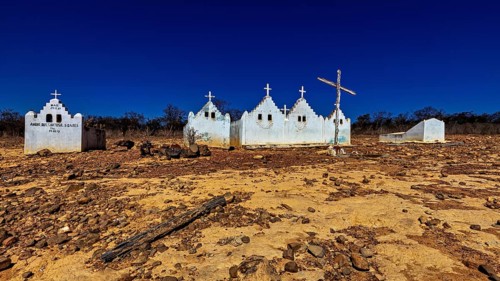 White chapels with crosses in a barren, dry desert landscape under blue skies, cemetery in the