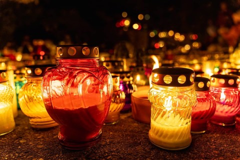 Heart-shaped candle among glowing candles in the night at cemetery on all saints day, day of the