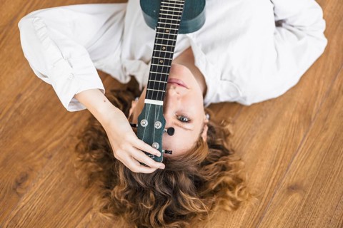 Woman with a ukulele on a wooden floor, giving a serene and introspective vibe