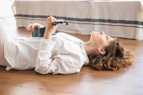 Person lies on a wooden floor with a ukulele, looking upward in a relaxed state