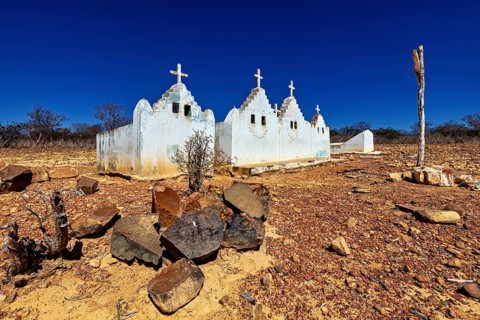 Small chapel with crosses on a dry, rocky area under a bright blue sky, cemetery in the thorny bush