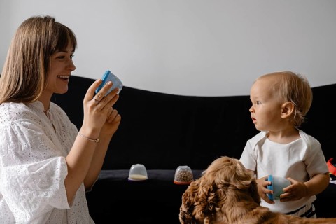 A mother and baby interact with colorful cups while a dog observes, highlighting playtime and