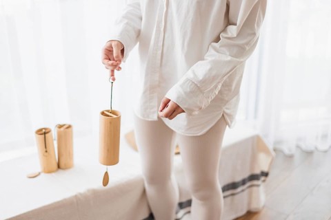 Person holding a bamboo wind chime in a bright room, dressed in white