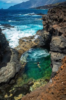 Woman enjoying a refreshing swim in a beautiful natural pool carved into volcanic rock formations