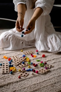 Person dropping colorful balls onto a mix of scattered wooden toys and balls