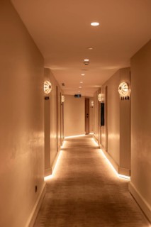 A well-lit hotel corridor with soft lighting and modern decor. The walls are painted in neutral