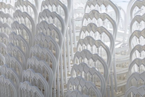 Stacked white plastic chairs create a uniform background texture. The chairs are arranged closely,