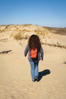 Long-haired curly-haired woman with a backpack walking on sand dunes, A woman with curly hair walks