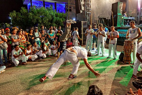 Capoeira dancers perform acrobatic movements at night, accompanied by drummers and spectators, The