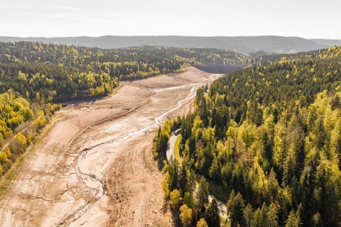 Long dry riverbed stretches between forests and hills, emptied Schwarzenbach dam, Forbach, Black