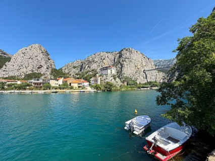 Boats are moored on the banks of a clear blue river, surrounded by tall rocks and colorful houses