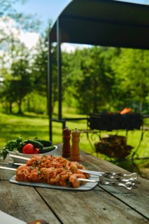 Marinated meat skewers and fresh vegetables on wooden picnic table near grill in backyard