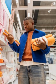 A man stands in a store holding orange towels in his hands. He looks at them with focus. The