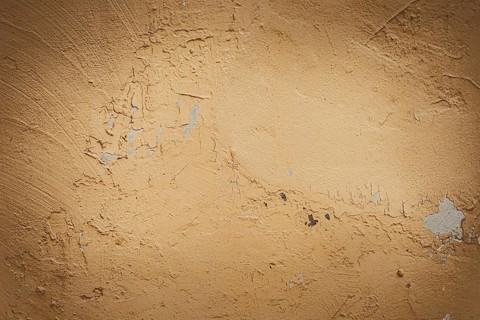 Textured beige wall with subtle imperfections and scratches. The surface appears weathered and