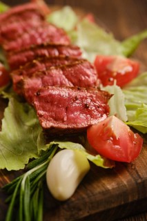 Beef steak cut into slices placed on bed of lettuce with fresh tomato slices and garlic. Displayed