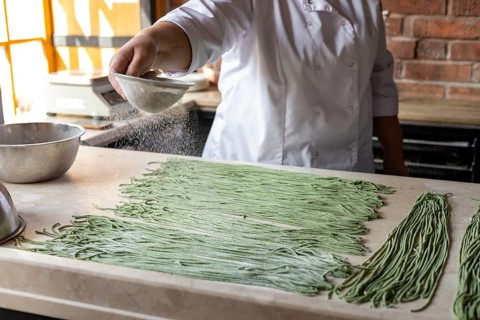 Woman sprinkles dough with sifted flour. Cook preparing handmade pasta. Woman's hands working with