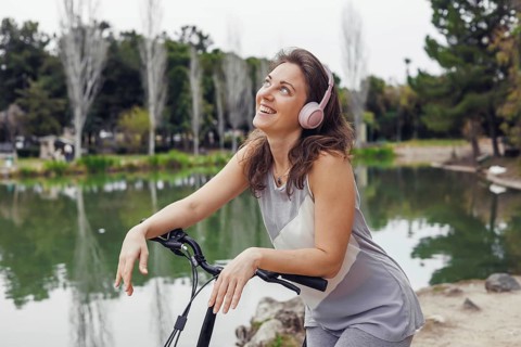 Young Caucasian woman with brown hair and pink headphones smiles while leaning on an electric