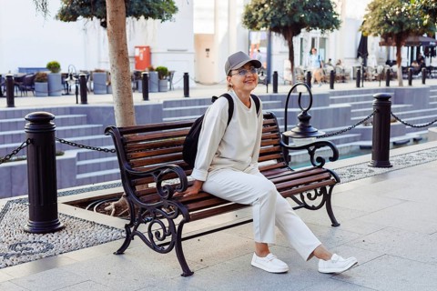 A cheerful middle-afed caucasian woman sits on a wooden bench, enjoying a sunny day in an outdoor