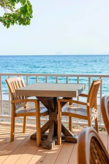 Brightly lit seaside dining space features wooden tables and chairs with stunning ocean views,