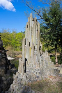 Massive, vertical stone column rises against a wooded background in the sun, at the Rakotz Bridge,