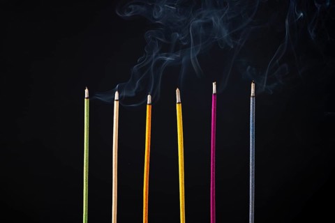 Six coloured incense sticks emit smoke, dark background