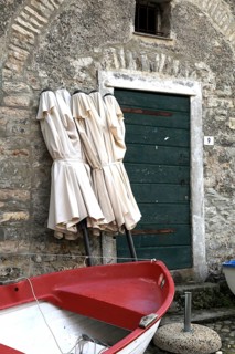 Rest in pre-season, folded umbrellas and a fishing boat ashore in front of a building. Tellaro,