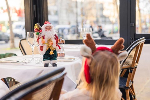 A young girl with blonde hair wearing reindeer antlers sits at a table. Christmas decorations