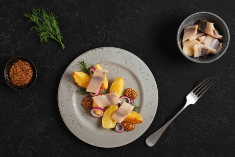 Plate with potato wedges arranged beside pieces of herring and decorated with mustard and onion.