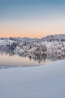 Dawn and sunrise at the wintry Forggensee in a snow-covered winter landscape in the foothills of