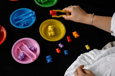 Colorful toy bears are being sorted into plates with tongs on a black background