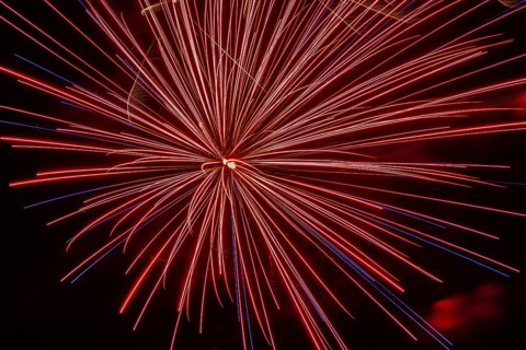 Red and blue illuminated trailing streaks of fireworks with zoom effect in black sky at night in