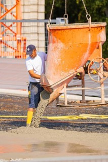 A construction worker pours concrete from a large orange hopper onto a surface, Parkhausbau, Calw,