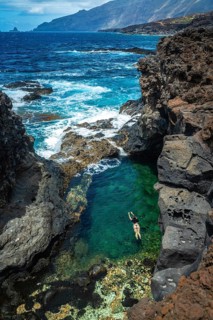 Woman enjoying swimming in a natural clear water pool formed by volcanic rocks and ocean waves