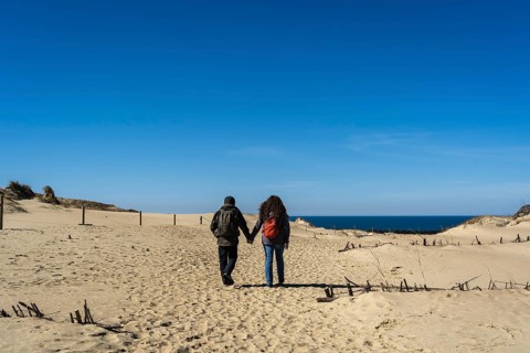 A couple of travelers with a backpack, hand in hand, walks along the sandy Dead Dunes, on the