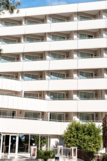 A modern hotel building with multiple balconies and large windows. The structure features a clean,