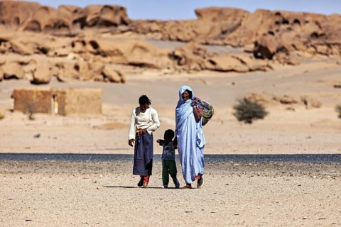 Family in traditional dress walking through a desert landscape with rocks in the background, woman