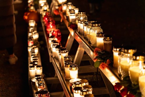Lit candles in glass holders glow on a multi tier metal structure at night, with red and orange