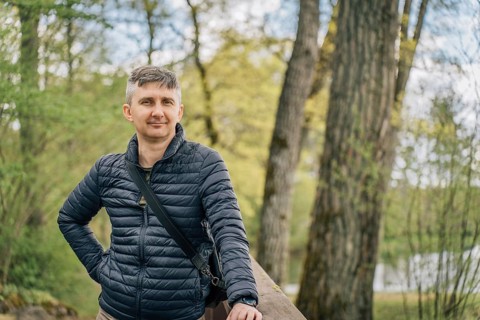 A middle-aged man with a gray hair in a thin down jacket in early spring surrounded by trees, A man