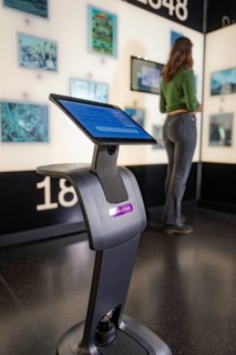 Interactive museum installation with display in the foreground and visitor looking at exhibits,