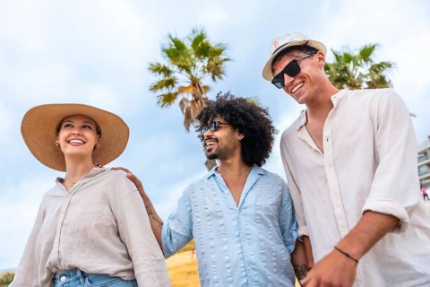 Diverse group of young friends smiling and walking along a sunny beach, enjoying a carefree summer