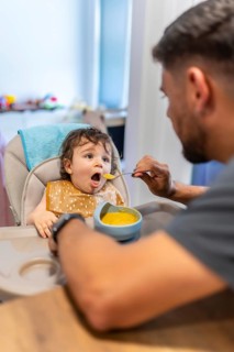 Young father lovingly feeding his adorable baby son nutritious vegetable puree while sitting in a
