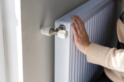 Close-up of a hand adjusting the temperature on a radiator thermostat, regulating home heating for
