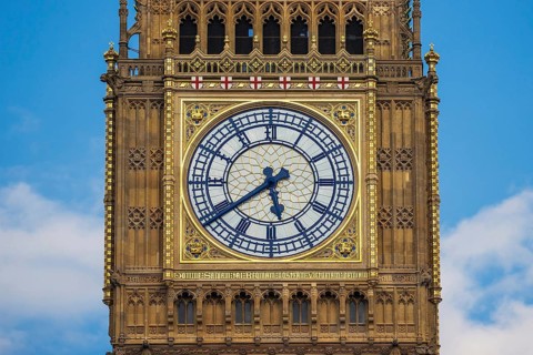 The ornate gilded clock face of the Elizabeth Tower stands out against a blue sky at the Houses of