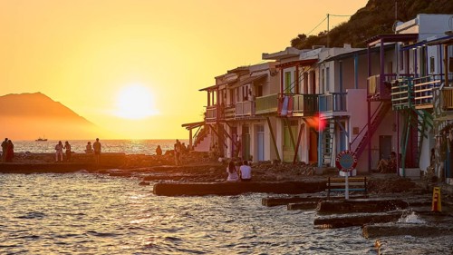 Colourful buildings along the coast at sunset with silhouettes of people and warm light,